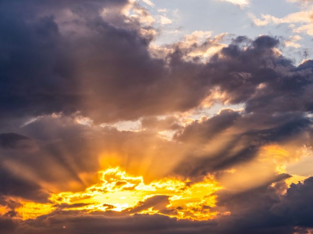 Dramatic golden rays of sunlight breaking through dark clouds, casting a warm glow across the sky at sunrise or sunset