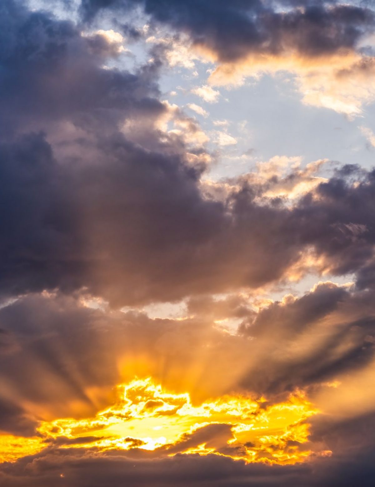 Dramatic golden rays of sunlight breaking through dark clouds, casting a warm glow across the sky at sunrise or sunset