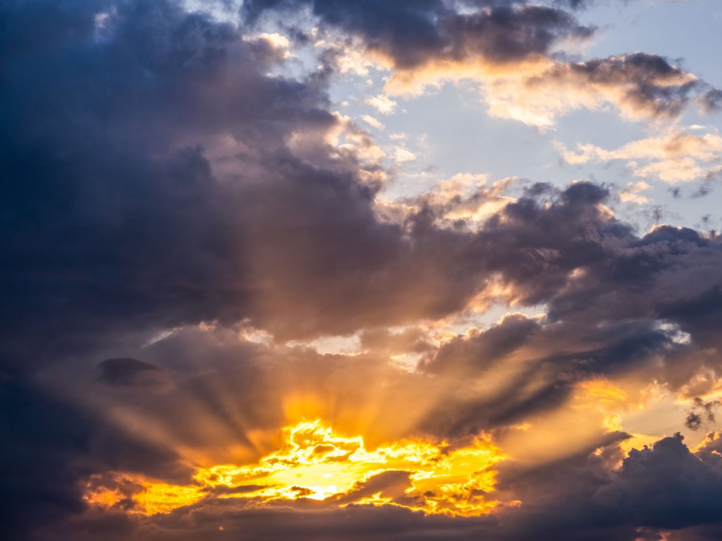 Dramatic golden rays of sunlight breaking through dark clouds, casting a warm glow across the sky at sunrise or sunset