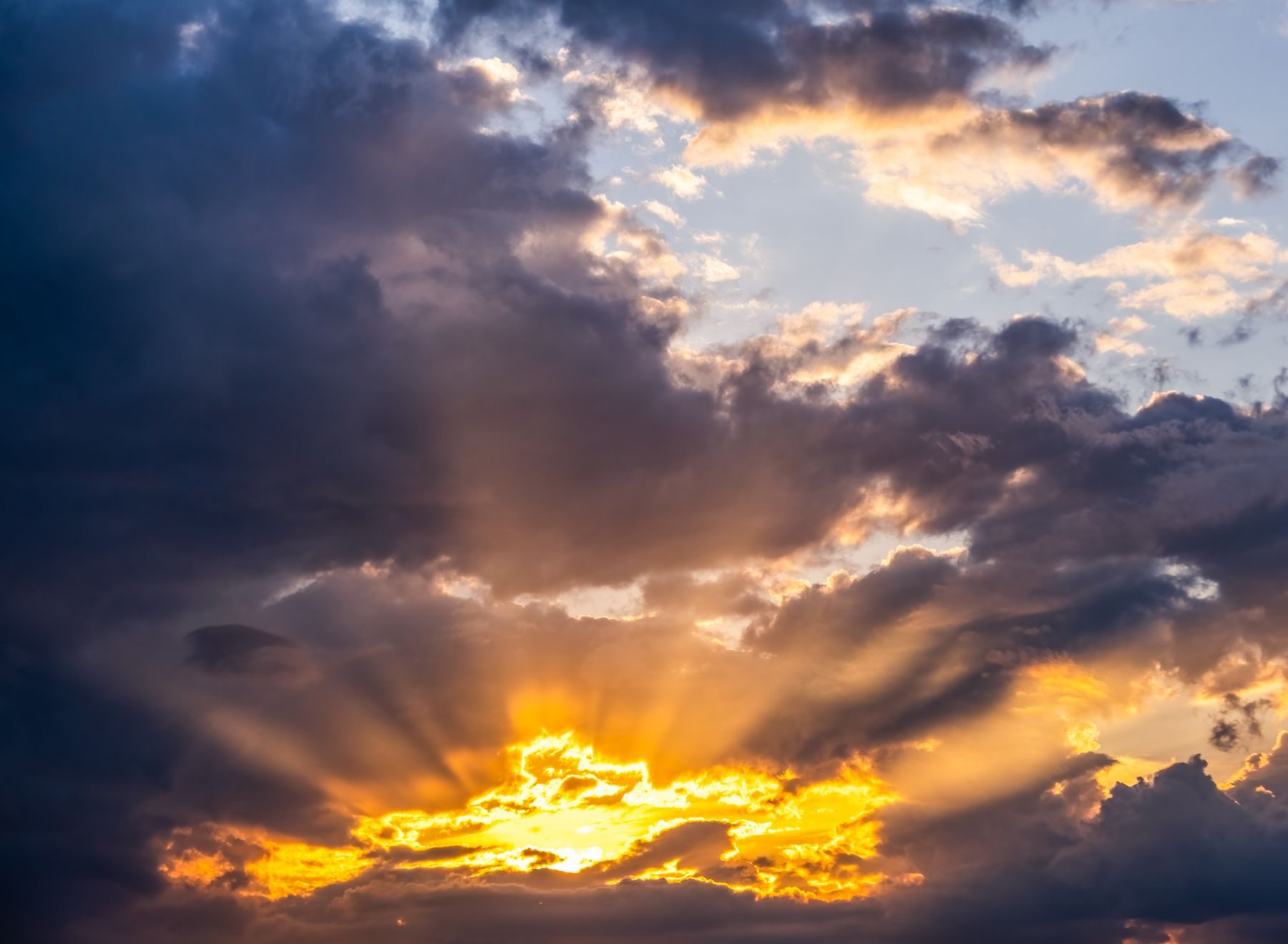 Dramatic golden rays of sunlight breaking through dark clouds, casting a warm glow across the sky at sunrise or sunset