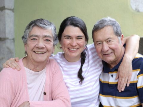 Smiling woman with her elderly parents, embracing and enjoying a happy moment together outdoors.