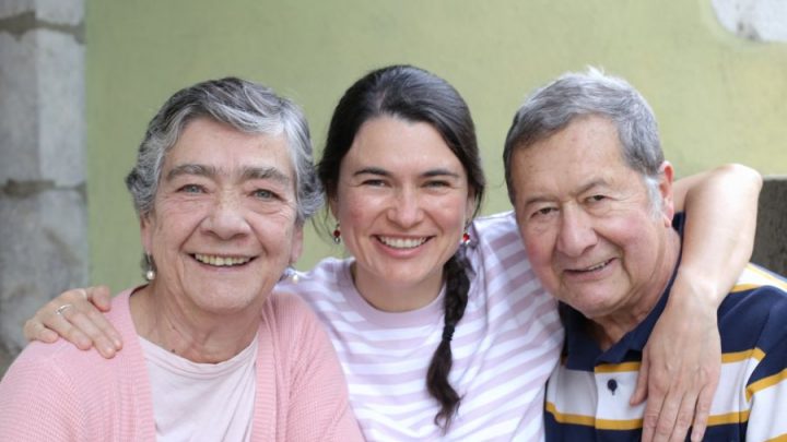 Smiling woman with her elderly parents, embracing and enjoying a happy moment together outdoors.