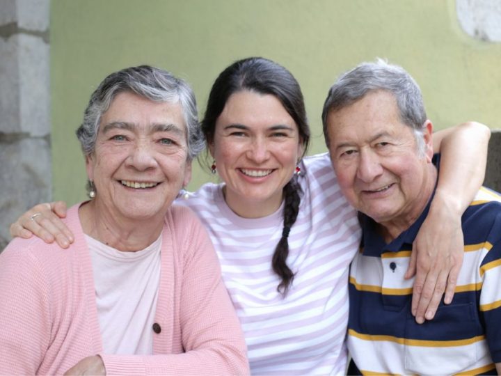 Smiling woman with her elderly parents, embracing and enjoying a happy moment together outdoors.