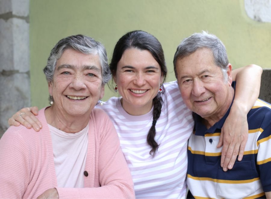 Smiling woman with her elderly parents, embracing and enjoying a happy moment together outdoors.