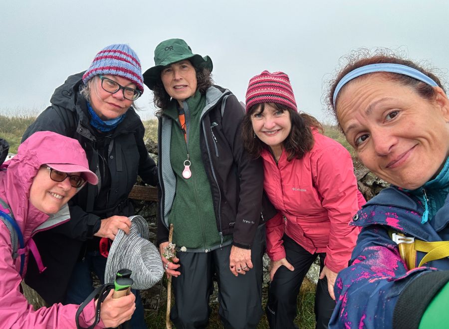 A group of five smiling hikers in colorful outdoor gear posing for a selfie on a misty day during their trek.