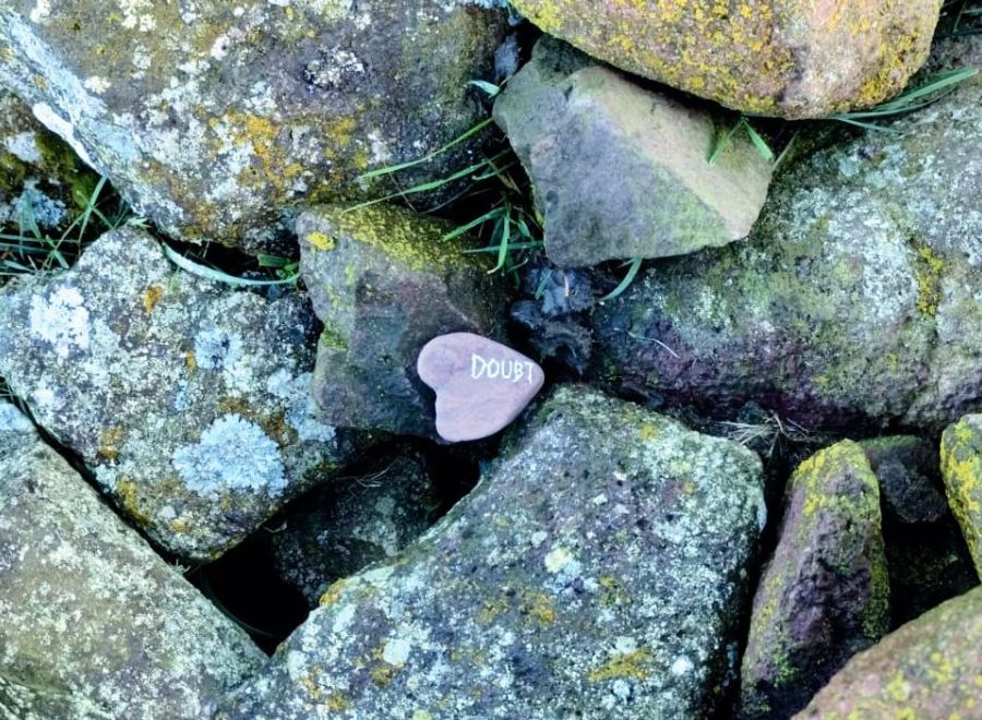 A heart-shaped stone with the word "DOUBT" written on it, placed among moss-covered rocks in a natural setting.