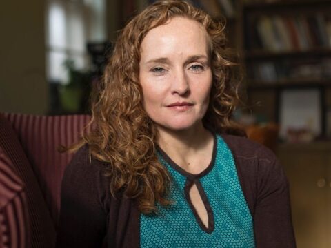 Caucasian woman with red hair in a blue shirt and sweater poses for a photo