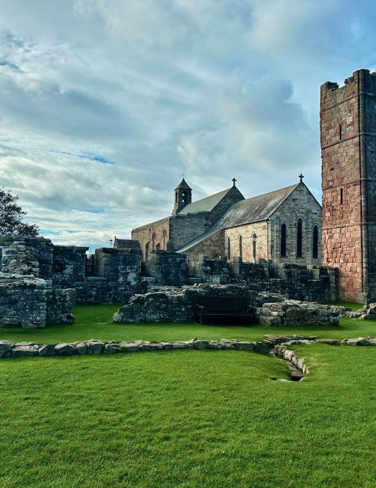 Ruins of an ancient monastery with a preserved church, lush green grass, and a cloudy sky in the background.