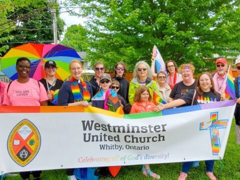 People hold up a banner with a rainbow that says Westminster United Church