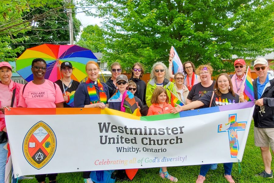 People hold up a banner with a rainbow that says Westminster United Church