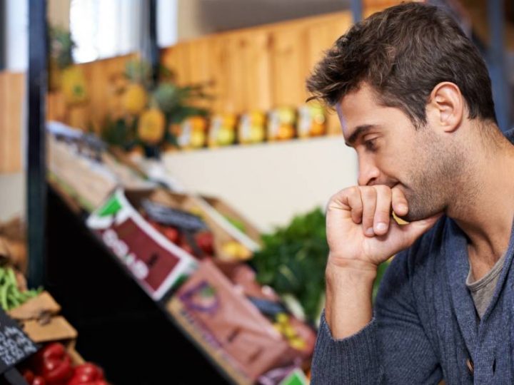 A man thoughtfully considers food options at a market, reflecting on ethical and sustainable eating choices.