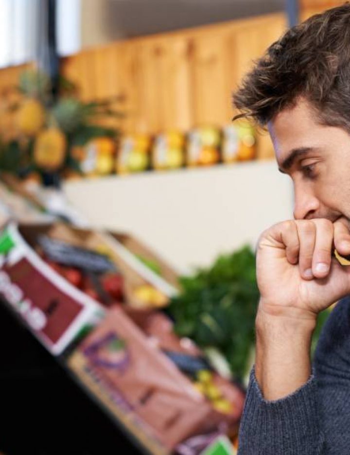 A man thoughtfully considers food options at a market, reflecting on ethical and sustainable eating choices.