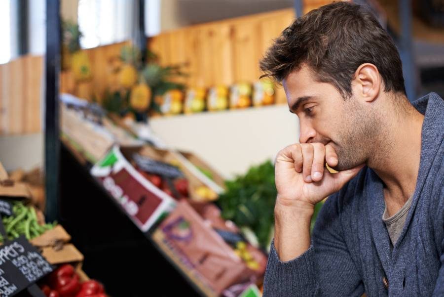 A man thoughtfully considers food options at a market, reflecting on ethical and sustainable eating choices.