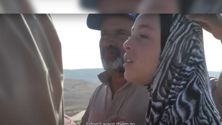 A brown-skinned man with a white beard and cap stands next to a hijabi woman. She is saying, "I don't want them to take my home," in subtitles.
