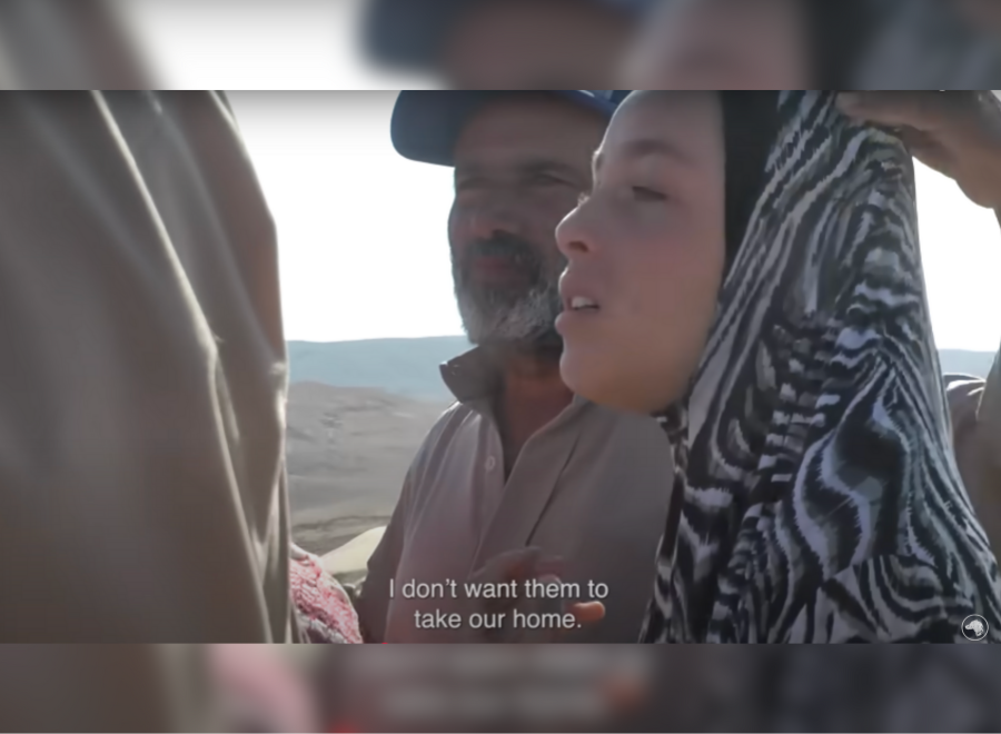 A brown-skinned man with a white beard and cap stands next to a hijabi woman. She is saying, "I don't want them to take my home," in subtitles.