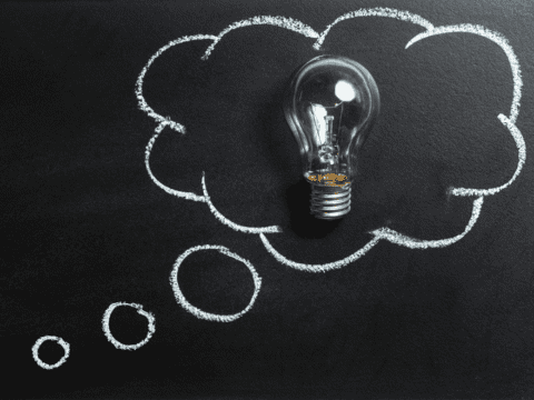 A lightbulb inside a drawing of a thought cloud against a black wall