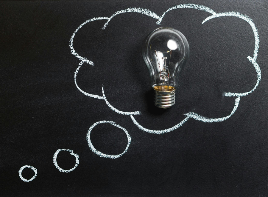A lightbulb inside a drawing of a thought cloud against a black wall
