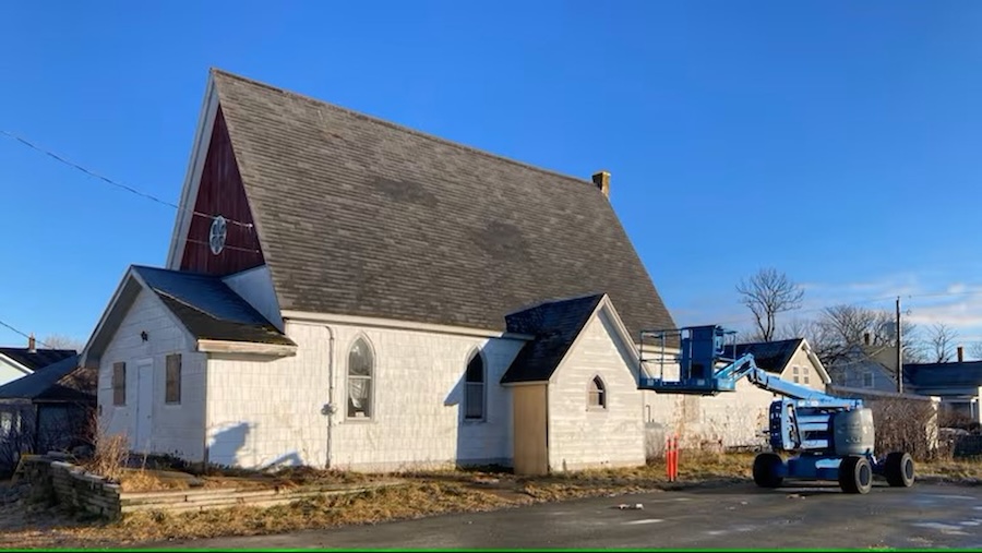 Image of a small church with a black roof, white walls standing against a blue sky