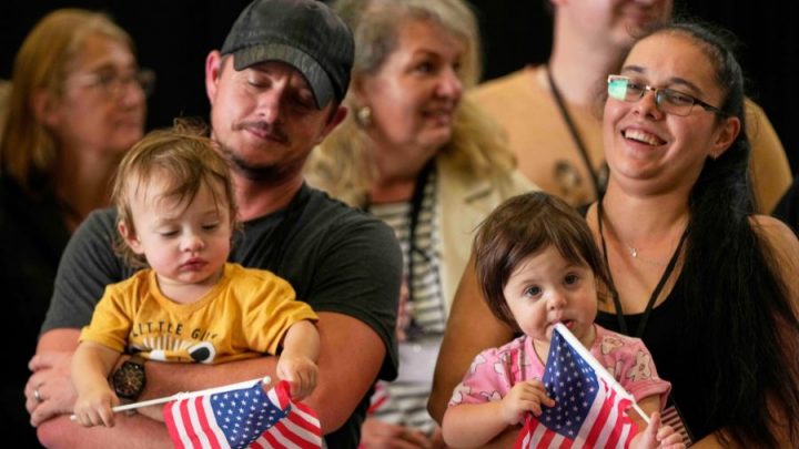 A man and a woman hold two toddlers, who holds American flags