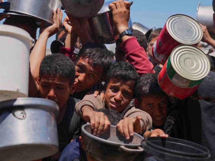 People, including children, crowd together, holding pots in front of them