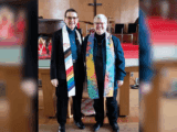Rev. Tammy Lindahl and Rev. Martha Juillerat stand side by side in their church, each wearing a colourful stole. Lindahl’s features a rainbow design, while Juillerat’s is a multicoloured tie-dye pattern. They’re smiling warmly at Esquimalt United Church.