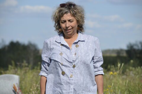An Indigenous woman is pictured outside, she wears a blue shirt, a necklace and sunglasses