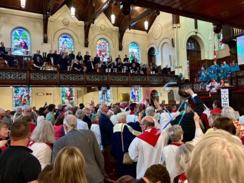 People stand in a church with stained-glass windows. Some wave ribbons