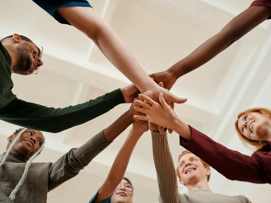 A team of people from diverse backgrounds reach out and put their hands on top of one another