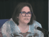 Moderator Carmen Lansdowne speaking into a microphone during the 45th General Council livestream, wearing glasses and a patterned top