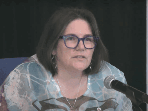 Moderator Carmen Lansdowne speaking into a microphone during the 45th General Council livestream, wearing glasses and a patterned top