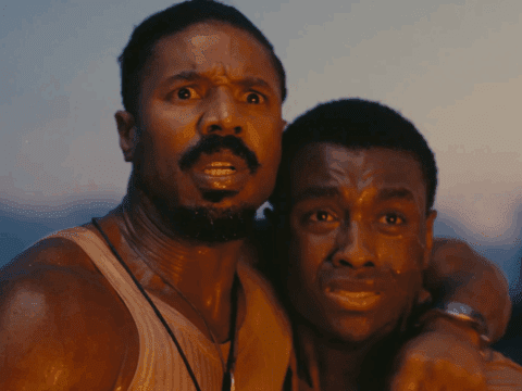 Two men, Smoke and Sammie, stand close together looking ahead with fear and shock. Smoke has his arm around Sammie, both of them sweaty and lit by a warm, sunset glow.