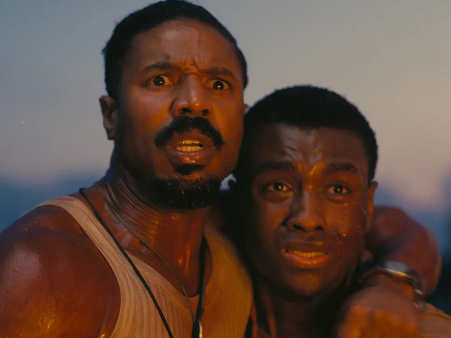 Two men, Smoke and Sammie, stand close together looking ahead with fear and shock. Smoke has his arm around Sammie, both of them sweaty and lit by a warm, sunset glow.