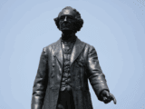 Image of a bronze statue of a man dressed in a petticoat with curls. He is pointing down with his index finger on his left hand