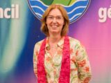 A Caucasian woman with shoulder-length red hair smiles for the camera while wearing a red stole and a flowered shirt.
