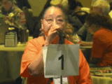 An Indigenous woman in an orange t-shirt speaks at a microphone