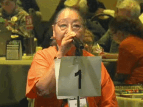 An Indigenous woman in an orange t-shirt speaks at a microphone