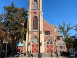 People sit on the steps of a older brick church