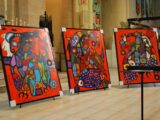 Three colourful paintings are seen propped up on a stage at a church