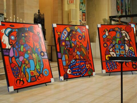 Three colourful paintings are seen propped up on a stage at a church