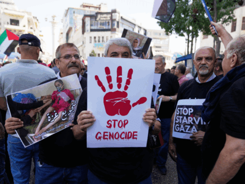A man holding up a white poster with a red hand print that says stop genocide underneath.