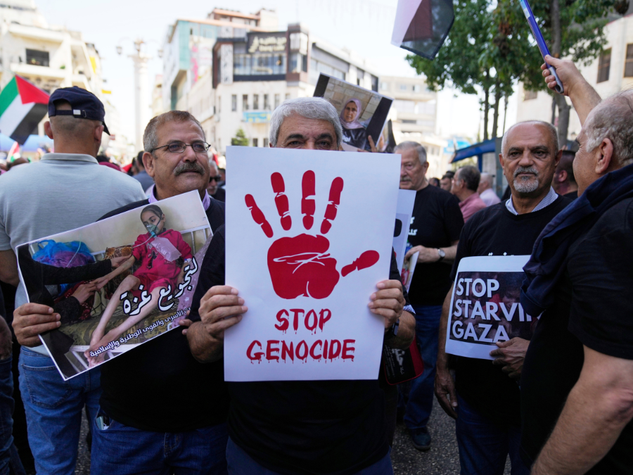 A man holding up a white poster with a red hand print that says stop genocide underneath.