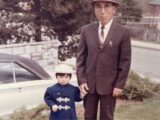 In this archival photo, a small Japanese child in formal wear stands beside an older man in a suit.