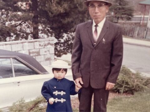In this archival photo, a small Japanese child in formal wear stands beside an older man in a suit.