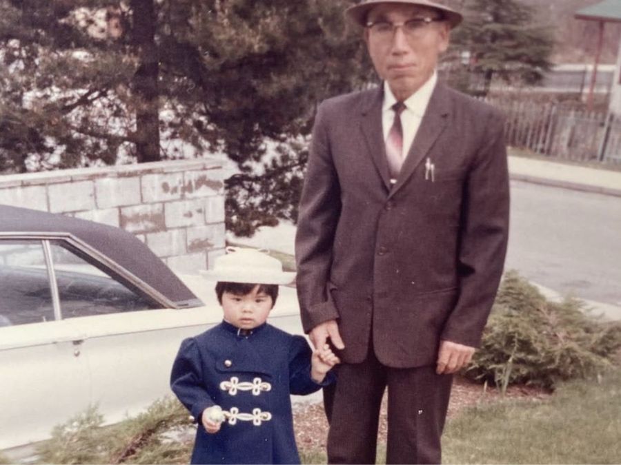 In this archival photo, a small Japanese child in formal wear stands beside an older man in a suit.