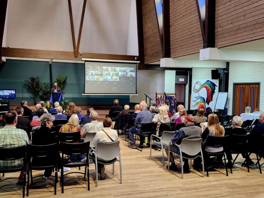 A congregation sits in chairs looking at a man speaking at the front