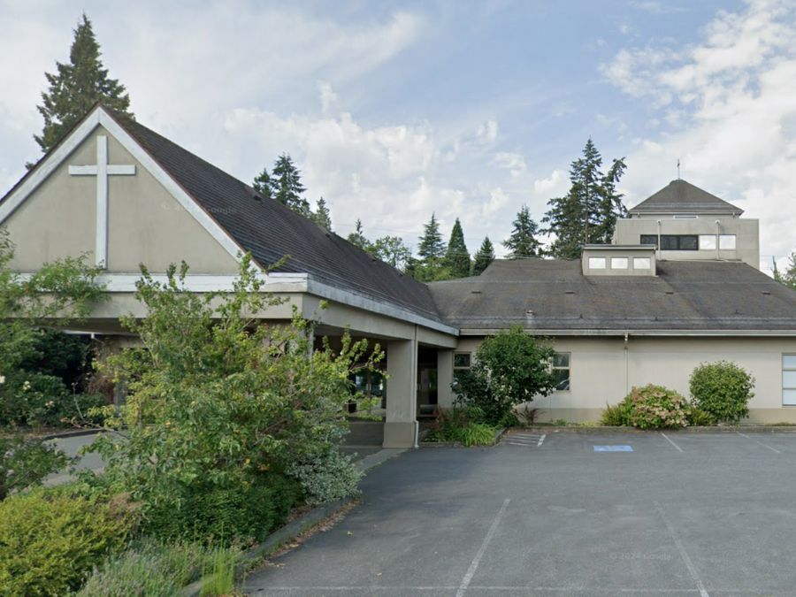 A modern church with a white cross at the front of its building and a parking lot.