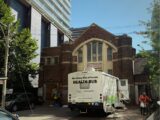 A old brick church is situated beside a very modern, tall, condo building.