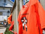 A large orange shirt that says "every child matters" is hung in front of an old wooden frame church.