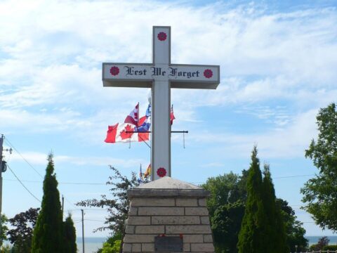 A white cross with the words Lest We Forget and designs of poppies is seen on top of a cairn