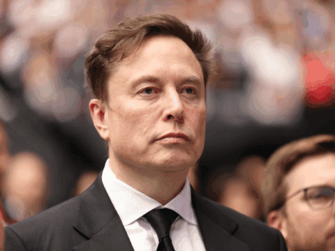Elon Musk in formal attire, looking focused in a blurred crowd setting.